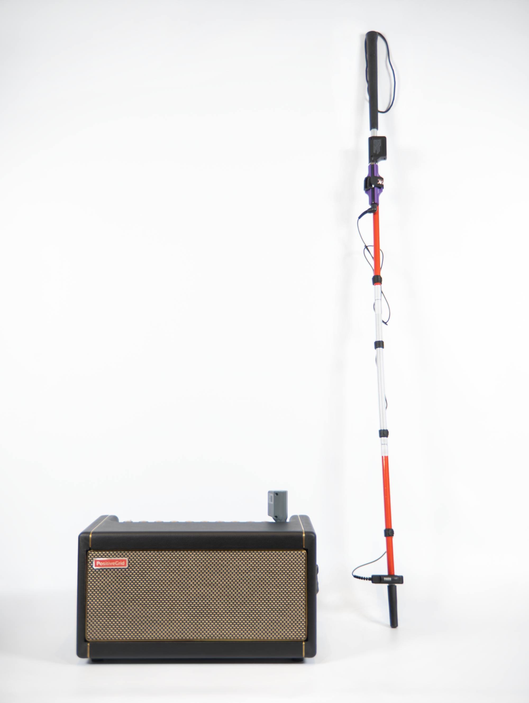 Leather and fabric modeling amplifier next to a vertical white cane with a contact microphone and wireless transmitter strapped to it