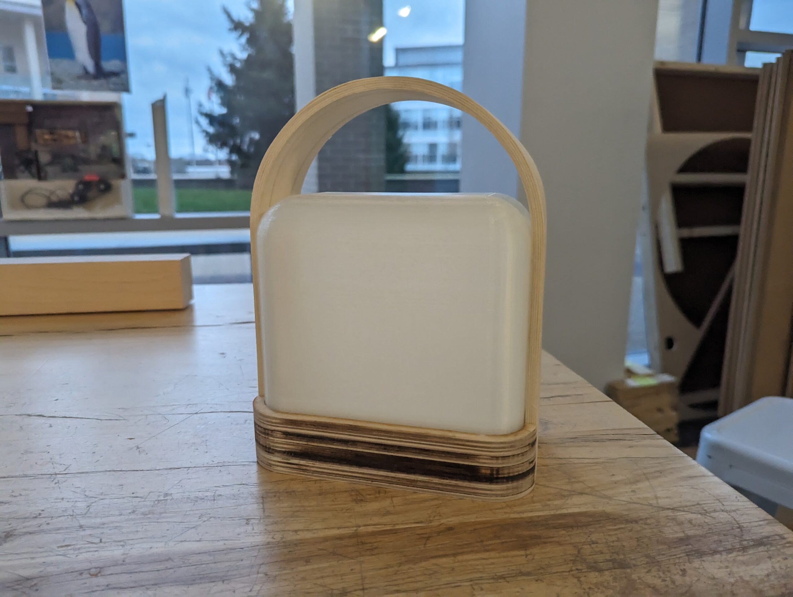 Wood and plastic lantern with exposed plywood layers sitting on wood workbench by a window