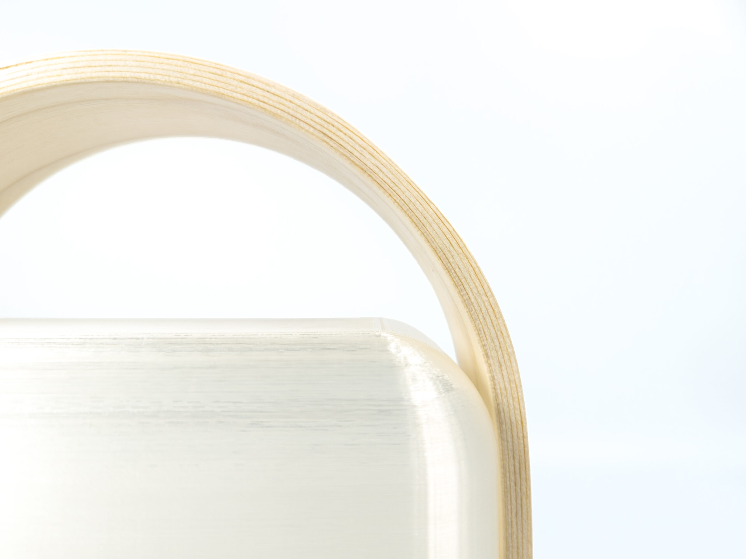 Closeup of layers of veneer stacked in a bent lamination to form a curved handle. Corner of plastic light diffuser and white background visible.