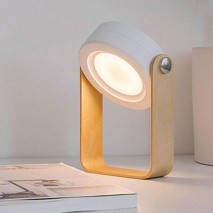 Cylindrical white light attached to bent wood 'U'-shaped stand sitting on white surface