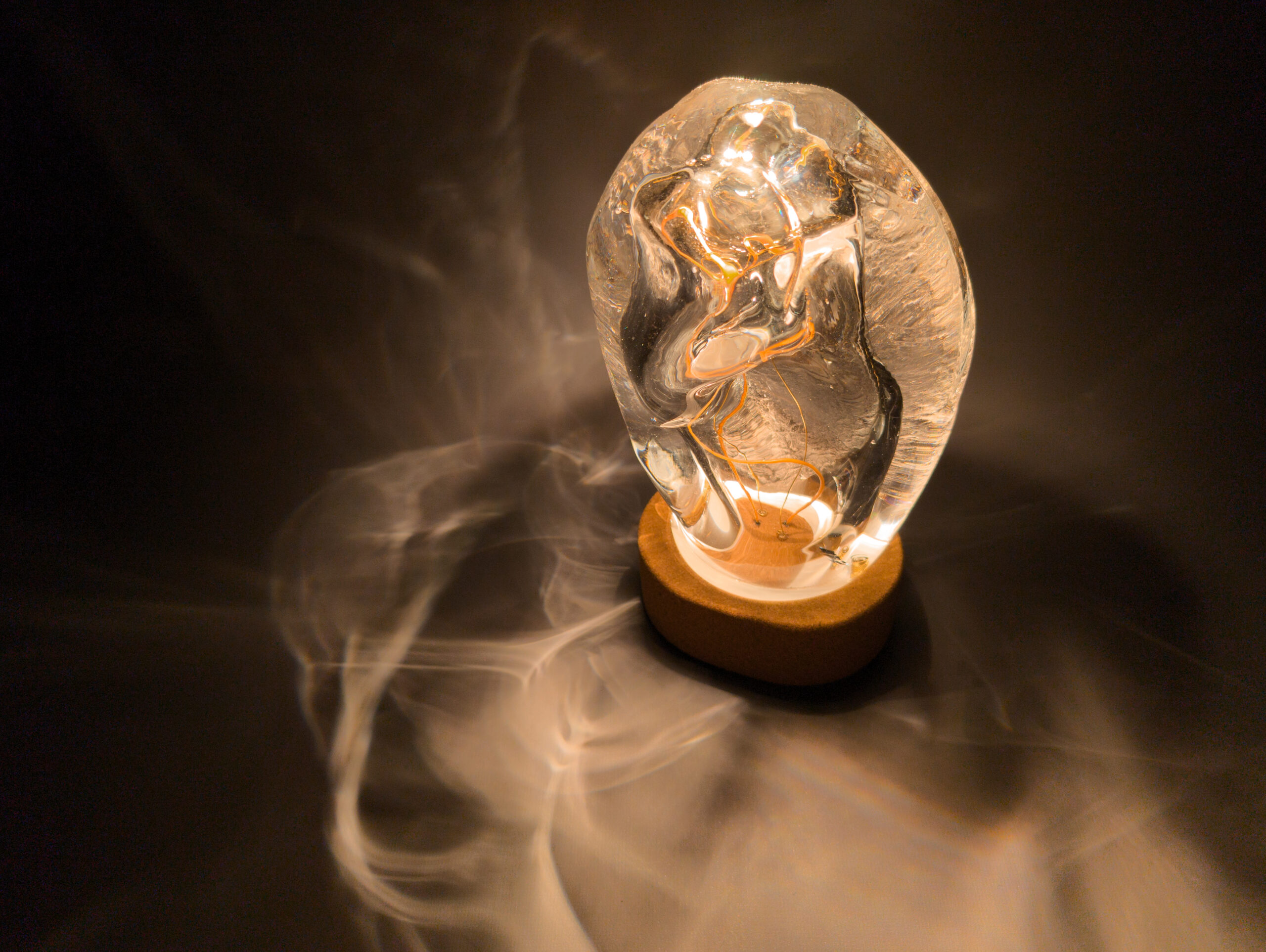 Light shining down onto organically-formed glass and cork sculpture and projecting wisps of light onto the table