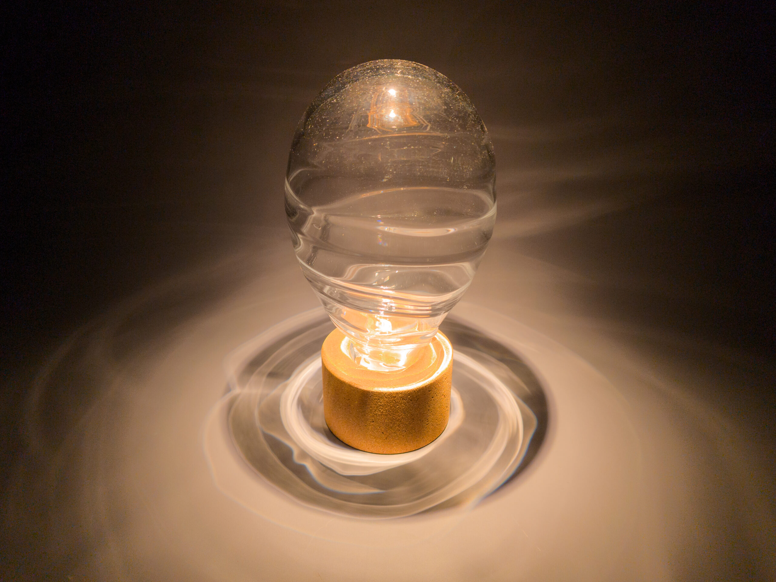 Light shining down onto blown glass and cork sculpture, projecting wavey rings of light onto the table