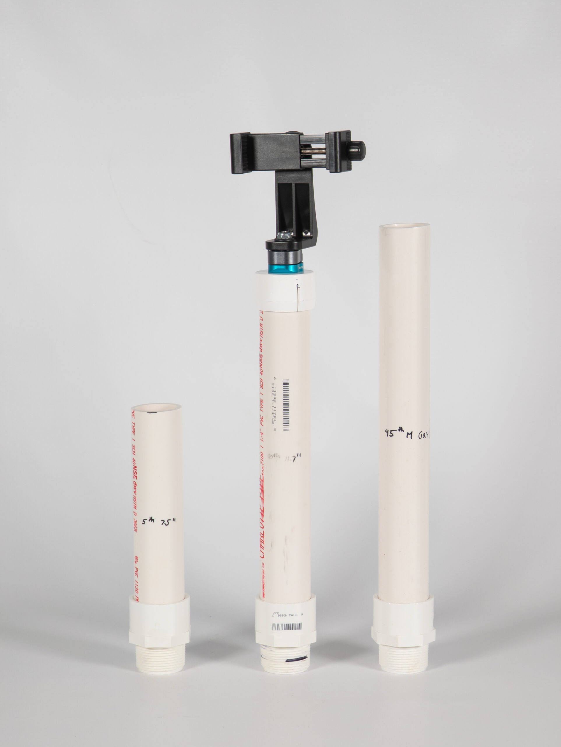 Three vertical PVC pipes with threading, one of white has a phone mount screwed into the top, standing against a white background.